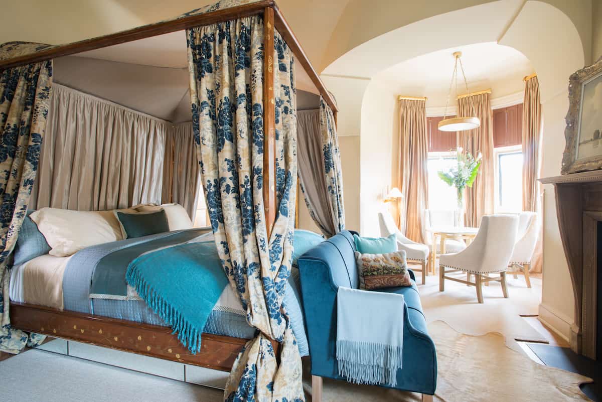 Perspective shot of Room Thirteen, dressed in blue and teal with a floral print to the four poster bed draping. This Mansion Room is situated on the corner of the building, bathing the turret side of this room in light.