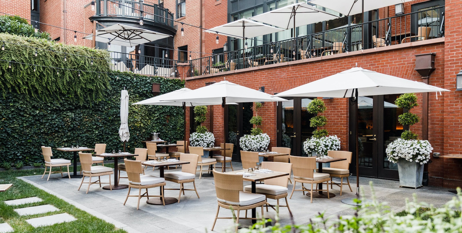 Tables, chairs and umbrellas set up in courtyard against lush ivy and brick face of the hotel.