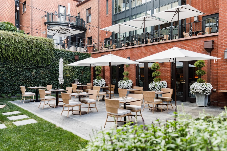 Tables, chairs and umbrellas set up in courtyard against lush ivy and brick face of the hotel.